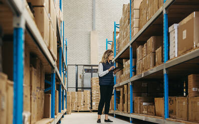 Female warehouse worker doing inventory control using warehouse management software. Logistics manager checking SKU's against an inventory list on a digital tablet. - JLPPF01346