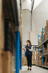 Warehouse worker doing inventory control using smart warehouse technology. Female logistics manager checking shipping labels against an inventory list on a digital tablet. - JLPPF01348