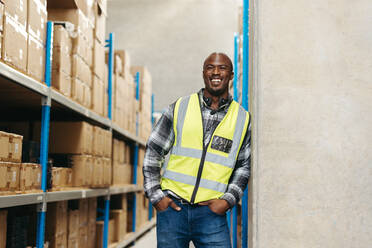 Happy warehouse order picker smiling at the camera with a headset around his neck. Cheerful warehouse employee working with voice-picking technology in a modern fulfilment centre. - JLPPF01365