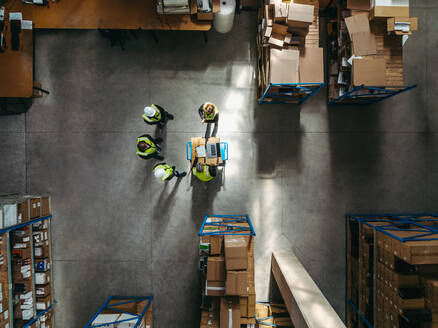 Aerial view of warehouse workers having a discussion during a staff meeting. Overheard view of a group of logistics employees working as a team in a large distribution warehouse. - JLPPF01377