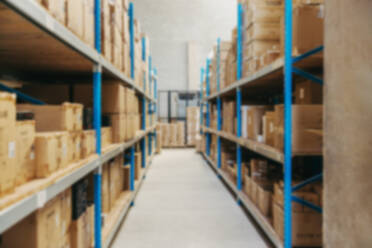 Defocused view of warehouse shelves filled with package boxes. Blurred background of a large distribution centre. - JLPPF01379