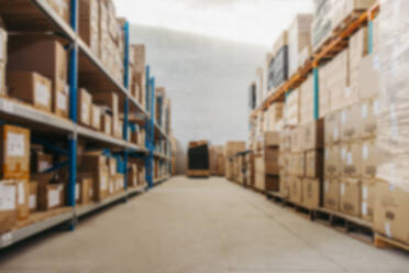 Blurred view of warehouse shelves filled with cardboard boxes. Defocused background of a large distribution centre. - JLPPF01380