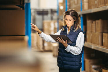 Eine Lagerarbeiterin sieht sich eine Inventarliste auf einem digitalen Tablet an. Ein Logistikmanager kontrolliert die Bestände mit Hilfe eines Lagerverwaltungssystems in einem Vertriebszentrum. - JLPPF01390