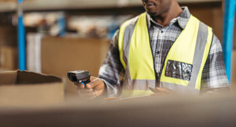 Male logistics manager scanning SKU's with a barcode reader in a distribution warehouse. Young black man doing inventory control in a modern fulfillment centre. - JLPPF01400