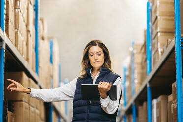 Warehouse worker checking SKU's against an inventory list on a digital tablet. Female warehouse employee doing stock control using a warehouse management system in a distribution centre. - JLPPF01409