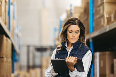 Eine Lagerarbeiterin sieht sich eine Inventarliste auf einem digitalen Tablet an. Eine Frau, die in einem modernen Distributionszentrum mit einem Lagerverwaltungssystem die Inventur kontrolliert. - JLPPF01411
