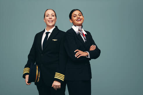 Ein glücklicher Pilot und eine Flugbegleiterin lächeln in die Kamera, während sie zusammen stehen. Ein fröhlicher Flugkapitän und eine Stewardess tragen ihre Uniformen vor einem Studiohintergrund. - JLPPF01506