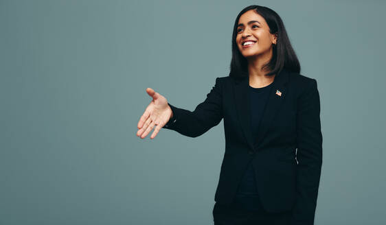 Freundliche Politikerin, die ihre Hand zum Händeschütteln in einem Studio ausstreckt. Eine Kongressabgeordnete der Vereinigten Staaten lächelt fröhlich, während sie vor einem Studiohintergrund steht. - JLPPF01515