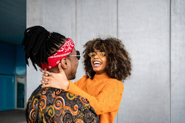 Back view loving African American modern man and woman embracing and smiling brightly against gray wall on street - ADSF39044