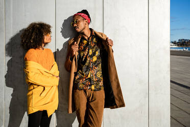 Full length of black African American couple in trendy vivid warm outfit standing with looking at each other on street - ADSF39072