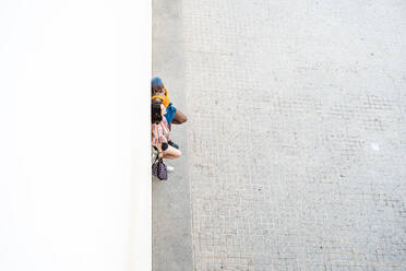 Von oben auf multiethnisches lesbisches Paar in modischer Sommerkleidung, das in der Nähe einer Mauer in einer städtischen Straße steht - ADSF39183