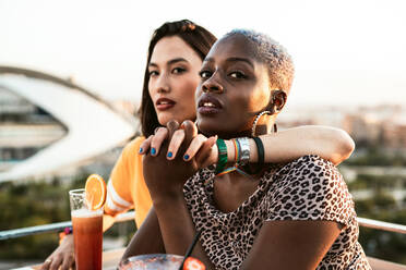 Stilvolle multiethnischen Freundinnen sitzen in Open-Air-Café umarmt und hält die Hände beim Genießen erfrischende Getränke auf verschwommenen Hintergrund - ADSF39208