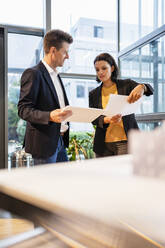 Smiling businessman showing tablet PC to businesswoman in office - DIGF18888