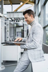 Smiling businessman using laptop at desk in industry - DIGF18903