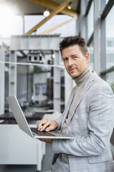 Mature businessman holding laptop standing in industry - DIGF18905