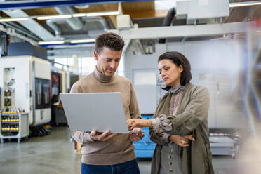 Businessman holding laptop discussing about machine installation with businesswoman in industry - DIGF18952