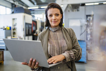 Lächelnde Geschäftsfrau mit Laptop in der Industrie - DIGF18957