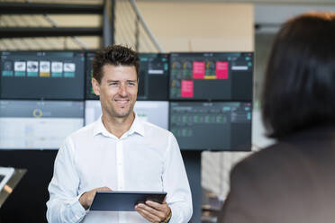 Smiling businessman holding tablet PC looking at businesswoman in industry - DIGF18969