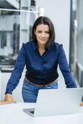 Smiling businesswoman with laptop on table in industry - DIGF18983