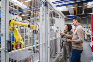 Businessman holding tablet PC explaining about robotic arm to businesswoman in industry - DIGF18991