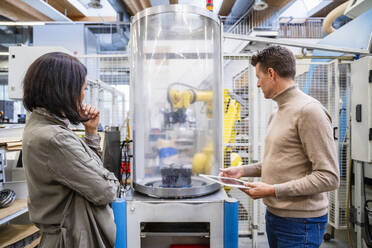 Businessman holding and businesswoman analyzing machine in industry - DIGF19007