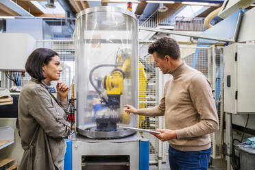 Businessman holding tablet PC discussing about machine with businesswoman in industry - DIGF19008