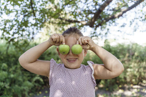 Glückliches Mädchen bedeckt Augen mit grünem Apfel im Park - TOF00136
