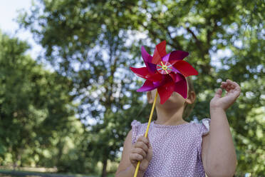 Girl covering face with pinwheel toy at park - TOF00143