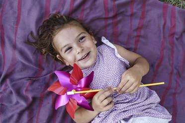 Happy girl holding pinwheel toy lying on blanket - TOF00147