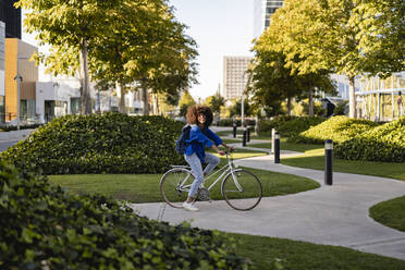 Smiling woman with bicycle on footpath at park - JCCMF07351