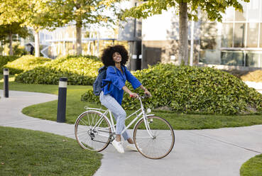 Lächelnde Afro-Frau mit Fahrrad auf dem Fußweg im Park - JCCMF07354