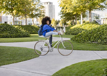 Fröhliche Frau auf einem Fahrrad im Park sitzend - JCCMF07355