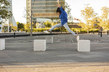 Carefree woman with arms raised jumping on concrete block - JCCMF07374