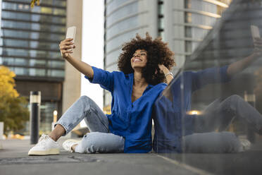 Lächelnde Afro-Frau, die ein Selfie durch ein an die Wand gelehntes Mobiltelefon macht - JCCMF07388