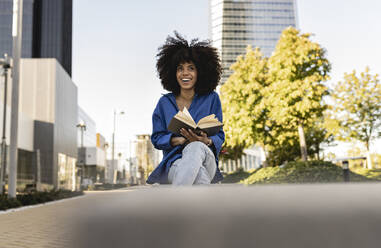 Glückliche Frau mit Afrofrisur hält Buch - JCCMF07408