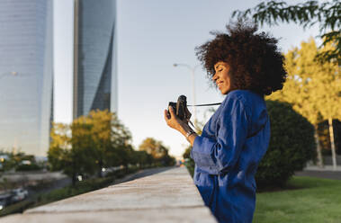 Smiling woman photographing through camera by wall - JCCMF07415