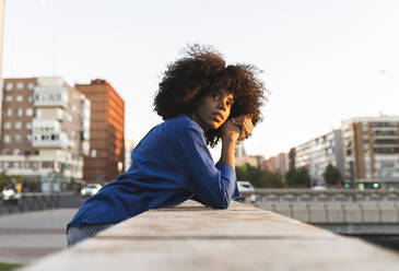 Thoughtful woman with Afro hairstyle leaning on wall - JCCMF07416
