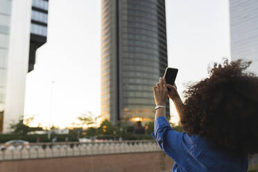 Frau fotografiert modernes Gebäude mit ihrem Smartphone - JCCMF07418