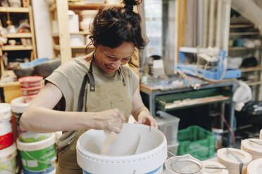 Fröhlicher Töpfer mit Eimer Ton bei der Arbeit in der Keramikwerkstatt - MRRF02447