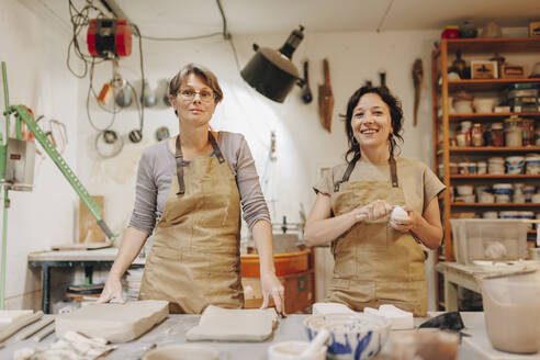 Happy entrepreneur with colleague working together at ceramics workshop - MRRF02465
