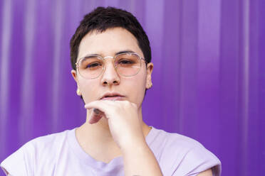 Nicht-binäre Person mit Brille vor lila Wellblechwand - EGCF00045