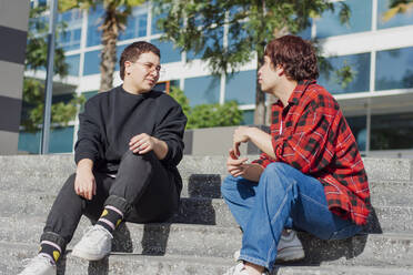 Nicht-binäres Paar sitzt zusammen auf einer Treppe vor einem Gebäude - EGCF00051