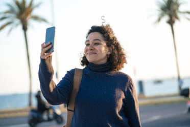 Lächelnde Geschäftsfrau, die ein Selfie mit ihrem Smartphone an einem sonnigen Tag macht - JOSEF13360