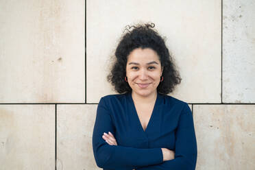 Smiling businesswoman with arms crossed standing in front of wall - JOSEF13374