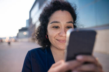 Smiling businesswoman using smart phone at footpath - JOSEF13381