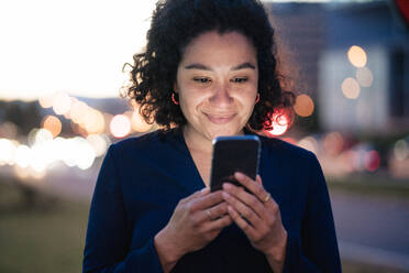 Smiling businesswoman using mobile phone at dusk - JOSEF13384