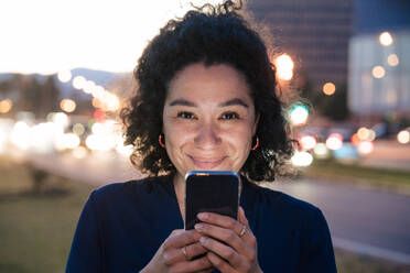 Lächelnde Geschäftsfrau mit Mobiltelefon in der Abenddämmerung - JOSEF13385
