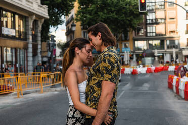 Seitenansicht eines sorglosen verliebten Paares in Freizeitkleidung, das auf der Straße steht und sich mit geschlossenen Augen zärtlich küsst - ADSF39233
