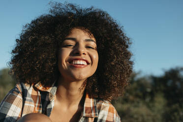 Inhalt Afroamerikanischer weiblicher Hipster in kariertem Hemd und mit Afrofrisur genießt den Sonnenuntergang und schaut in die Kamera - ADSF39277