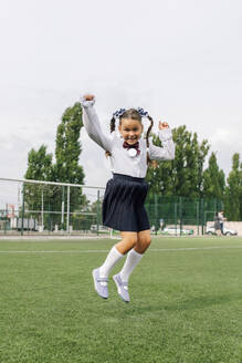 Unbekümmertes Mädchen in Schuluniform, das auf dem Schulrasen springt - JBUF00001